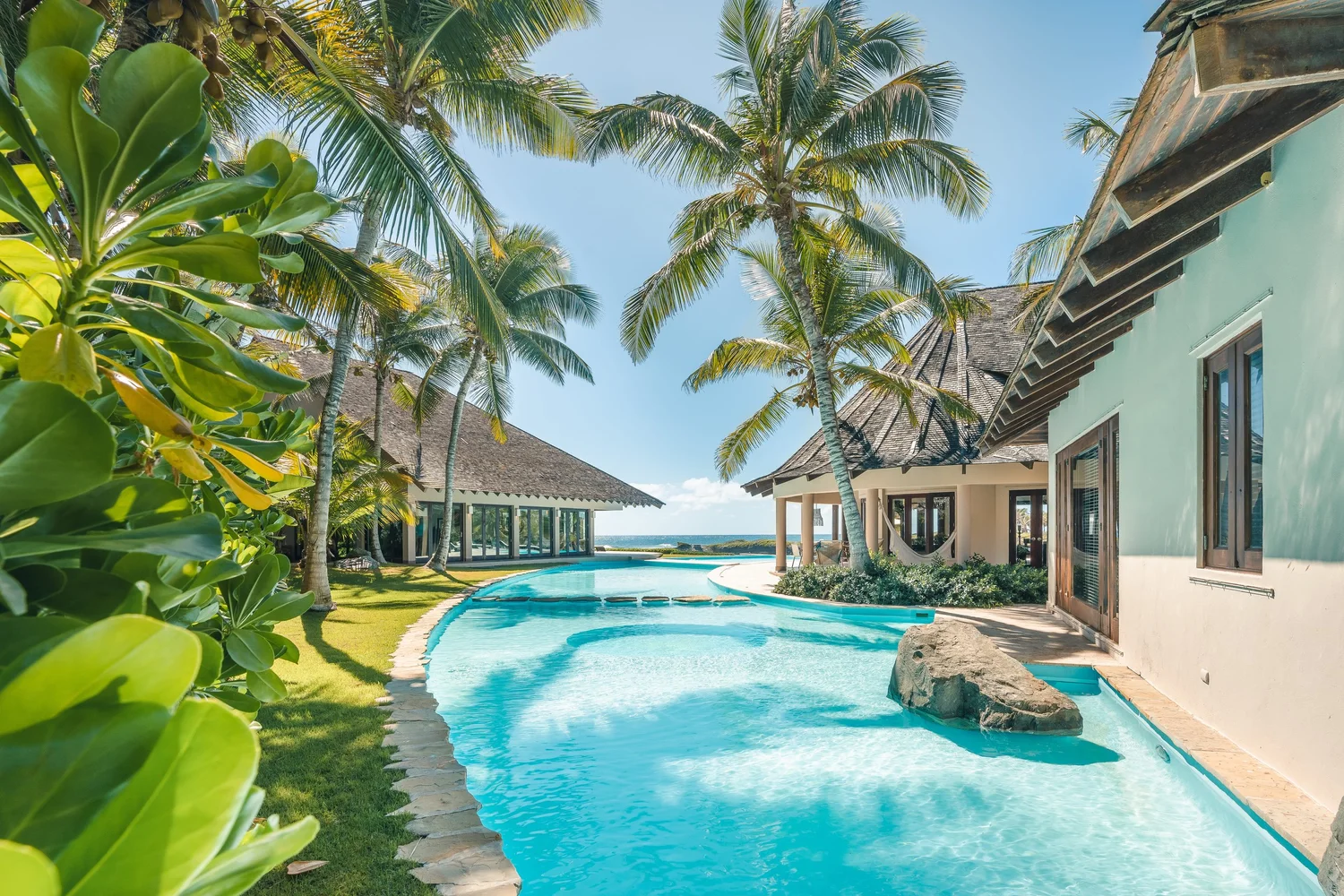 Winding turquoise pool between palm trees and bungalow-style villas on a sunny tropical resort.