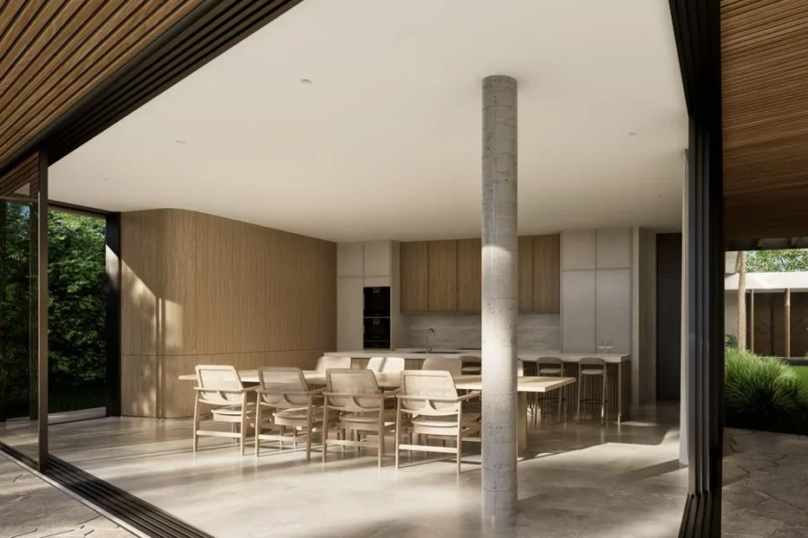 Open-plan kitchen and dining area with a long wooden table and chairs, a concrete pillar in the center, and sliding doors.